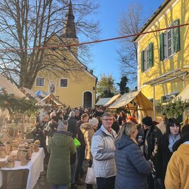 A bustling market with numerous stalls and many visitors. In the background, a church and a yellow building can be seen. | © Carina Sammer