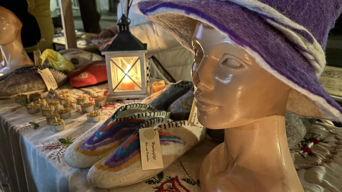 Ein Schaufenster mit einer klassischen Modepuppe, die einen lila Filzhut trägt. Im Hintergrund sind handgefertigte Schuhe und andere Waren auf einem Tisch ausgestellt. | © Oststeiermark Tourismus