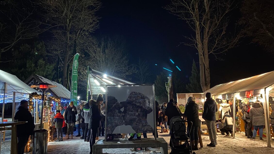 Ein belebter Weihnachtsmarkt bei Nacht mit festlicher Beleuchtung. Menschen stehen an verschiedenen Ständen und genießen die Atmosphäre. | © Oststeiermark Tourismus