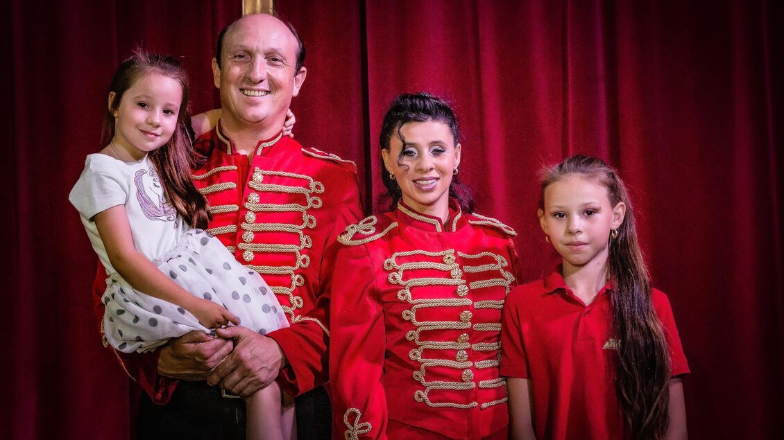 Ein Familienfoto von drei Personen in roten Kostümen vor einem roten Vorhang. Eine kleine Mädchen sitzt auf dem Arm eines Mannes, während zwei Frauen neben ihnen stehen. | © Circus Aros
