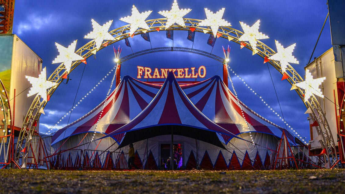 Rot-blaues Zirkuszelt des Circus Frankello mit beleuchtetem Sternenbogen und Schriftzug bei Dämmerung in Seiersberg-Pirka. | © Circus Frankello-Lukas Arnold