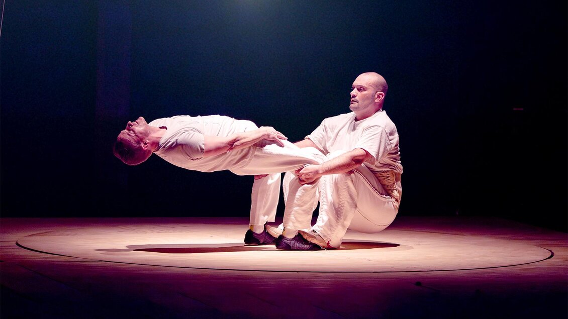 Zwei Akrobaten in weißer Kleidung zeigen bei Cirque Noël in Graz eine Balancefigur auf einer runden Bühne. | © Frank Emmers