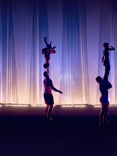 Vier Akrobatik-Duos zeigen bei Cirque Noël in Graz Hebefiguren und Handstände auf einer violett beleuchteten Bühne. | © Daniel Boud