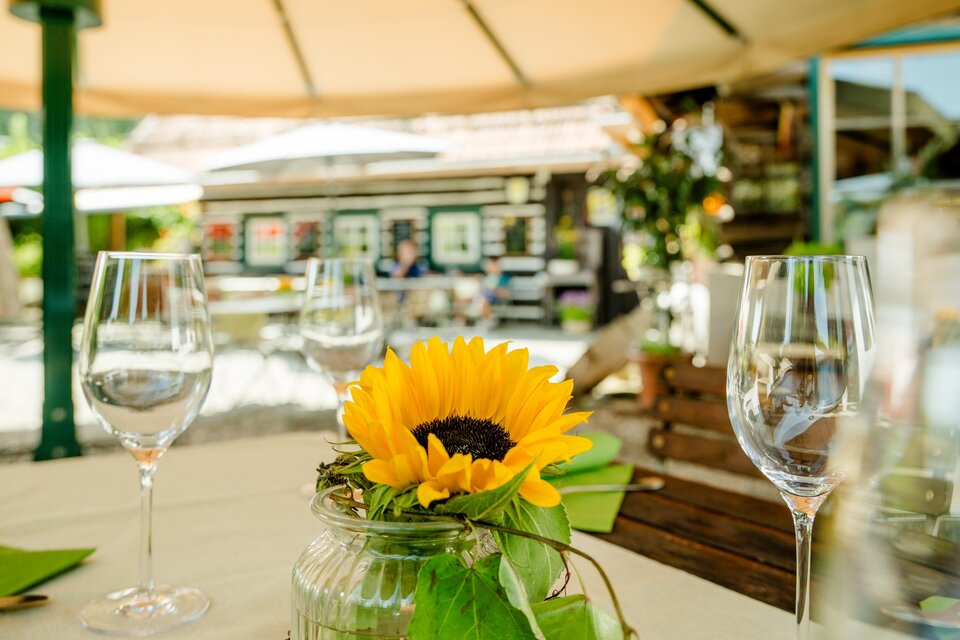 Sonniger Tisch mit Sonnenblume und Weingläsern im Gastgarten von Herbert's Stubn bei Graz. | © Region Graz-Mias Photoart