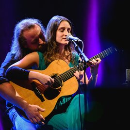 A duo performs on a stage. The singer plays guitar and sings, while her partner supports her. | © Kulturforum Bad Radkersburg