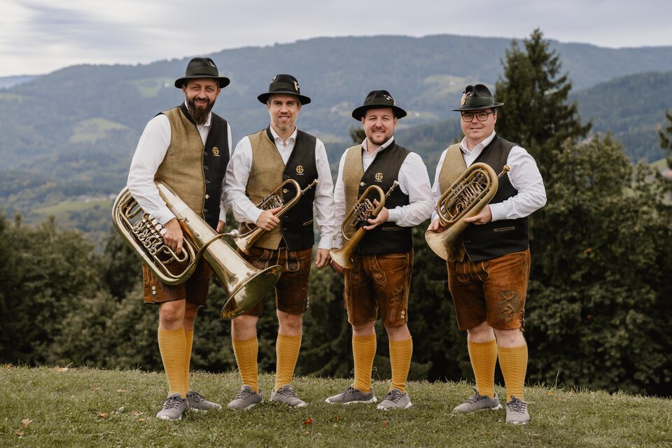 Blasmusikensemble in Tracht mit Hörnern und Tuba vor sanfter Hügellandschaft – musikalische Tradition und Naturgenuss beim Curkonzert in Bad Gleichenberg. | © Blechspann