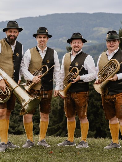 Blasmusikensemble in Tracht mit Hörnern und Tuba vor sanfter Hügellandschaft – musikalische Tradition und Naturgenuss beim Curkonzert in Bad Gleichenberg. | © Blechspann