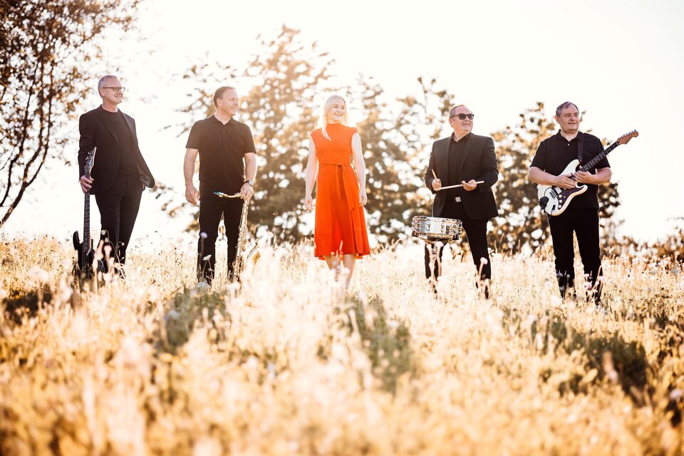 Band "Simply the PPest" mit Sängerin Petra Fritz-Fauland im roten Kleid in sommerlicher Wiesenlandschaft – musikalische Leichtigkeit und Lebensfreude beim Curkonzert in Bad Gleichenberg. | © Simply the PPest