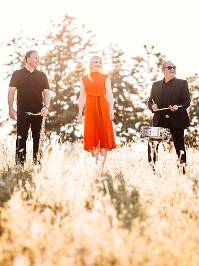 Band "Simply the PPest" mit Sängerin Petra Fritz-Fauland im roten Kleid in sommerlicher Wiesenlandschaft – musikalische Leichtigkeit und Lebensfreude beim Curkonzert in Bad Gleichenberg. | © Simply the PPest