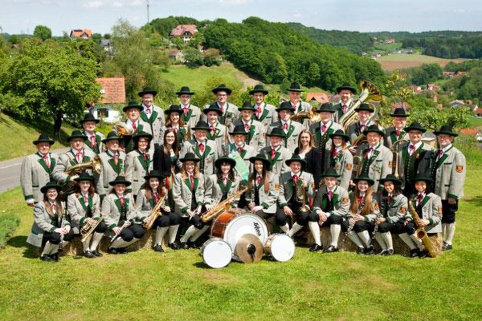 Trachtenmusikkapelle Gossendorf in traditioneller Uniform vor südoststeirischer Hügellandschaft – gelebte Blasmusik und starke Gemeinschaft in der Erlebnisregion Thermen- & Vulkanland.