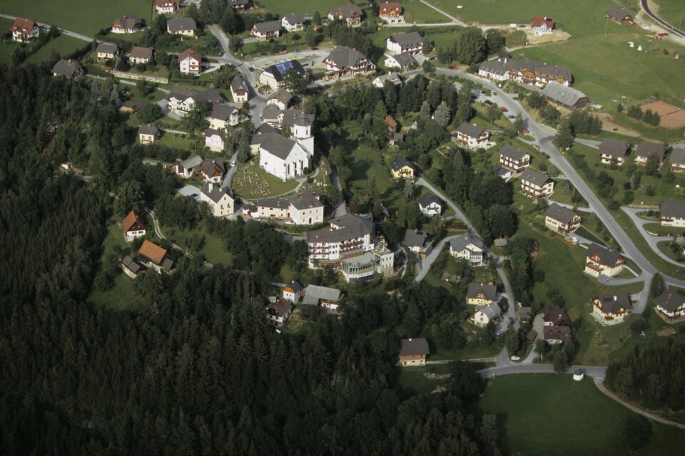 Eine Luftaufnahme eines kleinen Dorfes, umgeben von grünen Wäldern und Wiesen. Im Zentrum steht eine Kirche, umgeben von mehreren Häusern und Straßen. | © Tourismusverband Oststeiermark