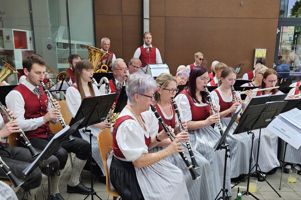 Eine Blaskapelle spielt draußen in traditioneller Kleidung. Die Musiker*innen konzentrieren sich auf ihre Instrumente und umgeben von Zuschauern. | © MG Lannach - Petru Rimovetz