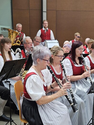 A brass band is playing outside in traditional clothing. The musicians are focused on their instruments and are surrounded by spectators. | © MG Lannach - Petru Rimovetz