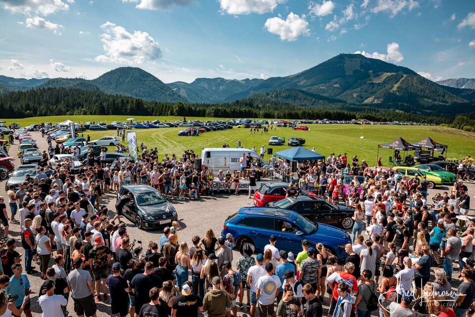 Ein großes Auto-Event mit einer großen Menschenmenge. Im Hintergrund sind grüne Berge und blue Himmel zu sehen. | © www.mariazell.blog