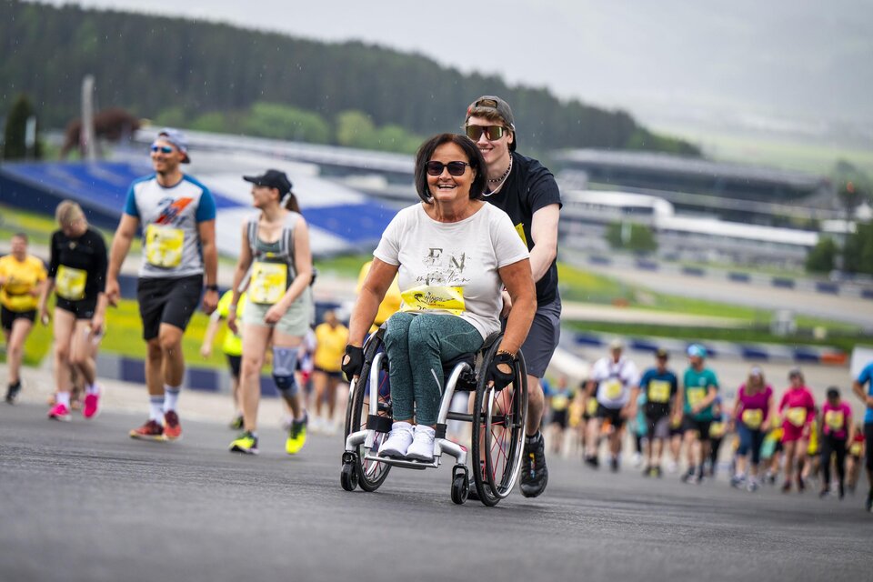 Ein Mann läuft fröhlich auf einer Rennstrecke unter einem Red Bull-Schild. Im Hintergrund ist ein Auto zu sehen, das sich auf der Strecke befindet. | ©  Lucas Pripfl Red Bull Ring
