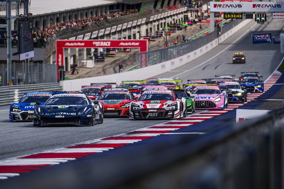 Ein spannendes Autorennen auf einer Rennstrecke mit mehreren Autos, die nebeneinander fahren. Im Hintergrund sind Zuschauer und Boxen zu sehen. | © Philip Platzer Red Bull Ring