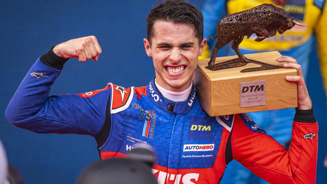 Ein junger Rennfahrer feiert seinen Sieg mit einer Trophäe in der Hand. Er trägt einen blauen Rennanzug und lächelt stolz in die Kamera. | © Red Bull Ring