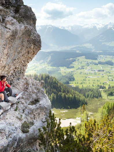 Eine Gruppe von Menschen sitzt auf einem Felsen mit Blick auf eine atemberaubende Berglandschaft. Im Hintergrund sind grüne Täler und schneebedeckte Gipfel zu sehen. | © Christoph Huber