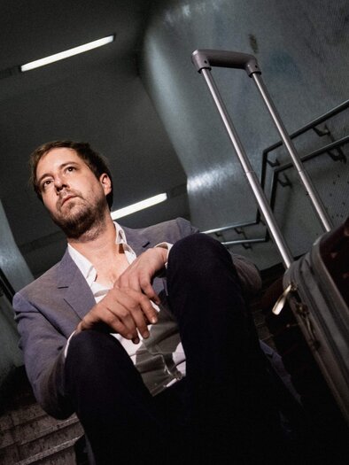 Ein Mann sitzt mit einem Koffer auf der Treppe eines U-Bahnhofes. Er schaut nachdenklich in die Ferne. | © Christopher Glanzl
