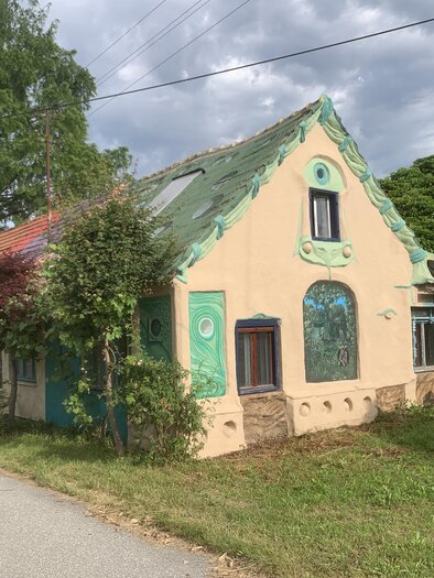 Künstlerisch gestaltetes Wohnhaus der Familie Liegle in Maierhofen mit farbenfrohen Fassadenmalereien und organischen Formen inmitten der Natur – außergewöhnliche Architektur, kreative Lebenskunst und kulturelle Vielfalt in der Erlebnisregion Thermen- & Vulkanland. | © Peter Liegle