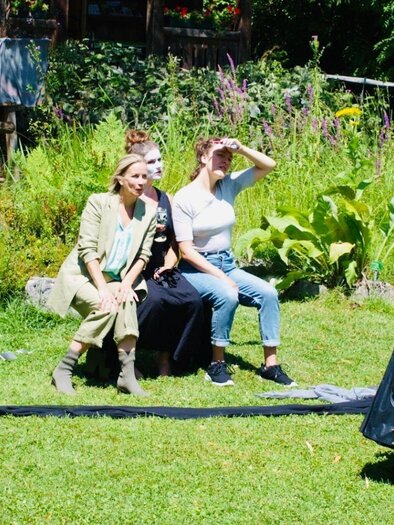 <p>Das Ensemble der Bluatschwitz Black Box führt im Garten voller Pflanzen eine Vorstellung auf. Einige Personen posieren, während eine andere Person in einem schwarzen Mante geradel spricht.</p> | © Bluatschwitzblackbox, bluatschwitzblackbox.eu/