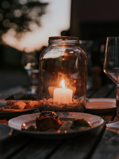 A festive table outdoors with candlelight and glasses. Delicious food is arranged on plates and the atmosphere is cozy. | © TVB Südsteiermark – Lukas Elsneg