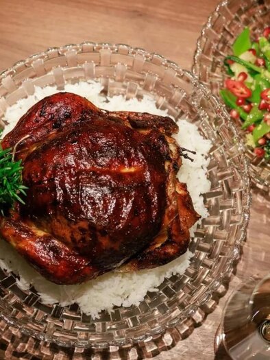 Ein gebratener Hühnchen auf einem Bett aus Reis, garniert mit frischen Kräutern. Daneben befindet sich ein bunter Salat mit Tomaten und Gurken. | © Martina Schmit