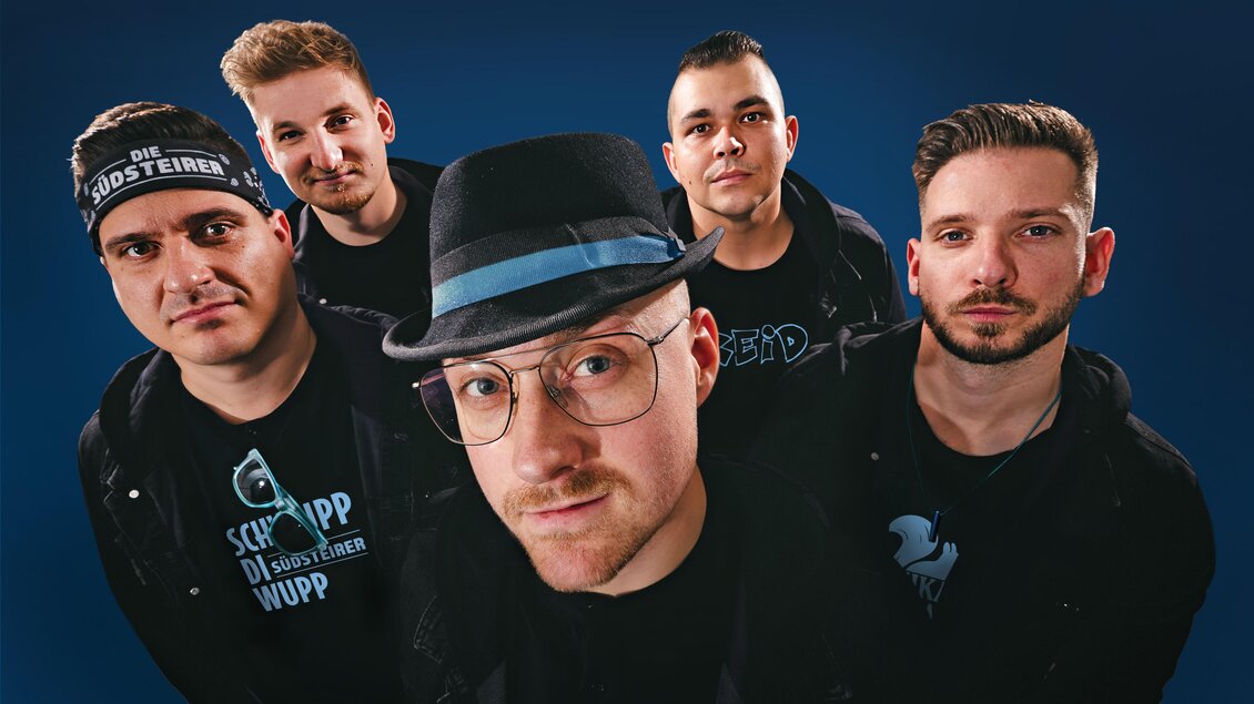 Eine Band mit fünf Mitgliedern posiert vor einem blauen Hintergrund. Alle tragen schwarze Kleidung und sehen selbstbewusst aus. | © Die Südsteirer