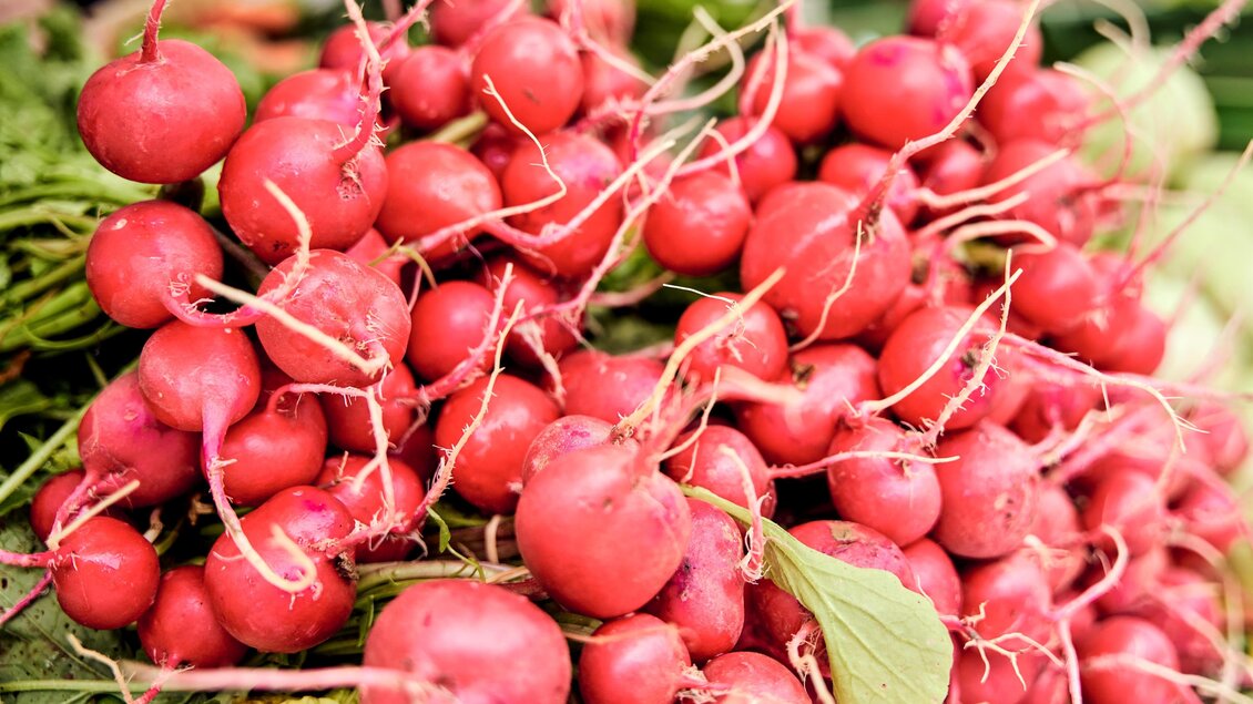 Frische, rote Radieschen liegen auf einem Markt. Sie sind mit grünen Blättern umgeben und sehen knackig aus.