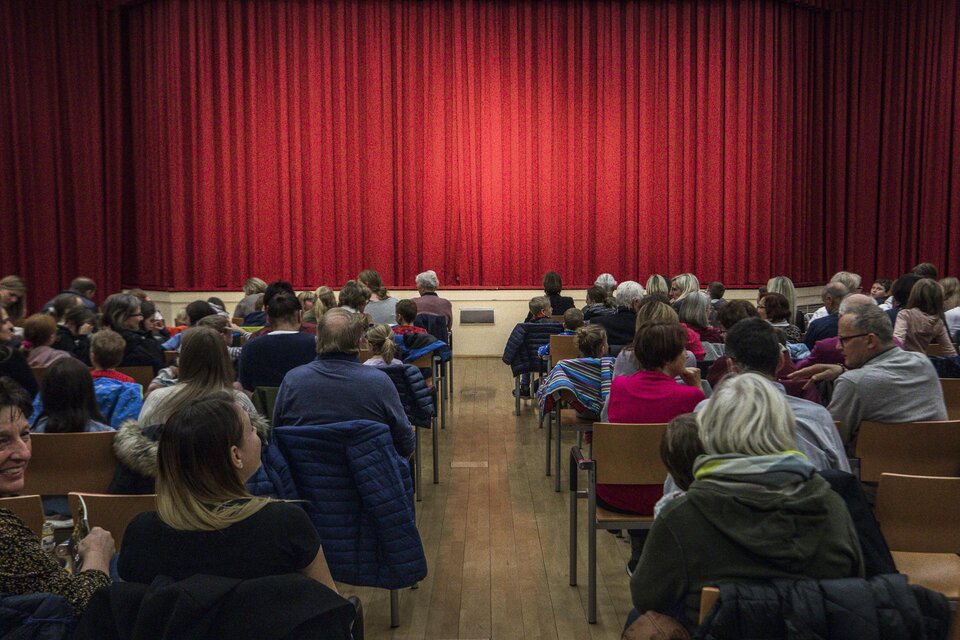 Ein voll besetzter Saal mit Menschen, die auf die Bühne schauen. Der rote Vorhang ist gespannt und wartet auf die Vorstellung. | © Tv Murau