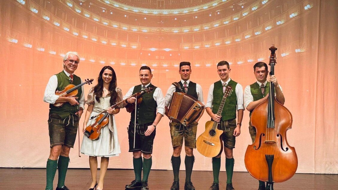 <p><p>Die Ausseer Bradlmusi mit 6 Musikanten und Musikantinnen, gekleidet in Tracht. Sie halten ihre Instrumente in der Hand und stehen fröhlich nebeneinander auf einer Bühne. </p> | © Ausseer Bradlmusi