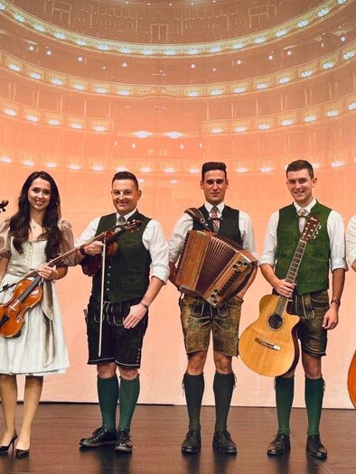 <p><p>Die Ausseer Bradlmusi mit 6 Musikanten und Musikantinnen, gekleidet in Tracht. Sie halten ihre Instrumente in der Hand und stehen fröhlich nebeneinander auf einer Bühne. </p> | © Ausseer Bradlmusi