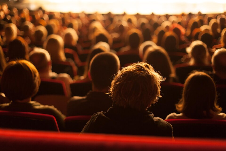 Ein Publikum sitzt in einem großen Saal und schaut auf die Bühne. Die Menschen sind in unterschiedlichen Positionen, und die Atmosphäre ist gespannt. | © AdobeStock_95665646.jpeg