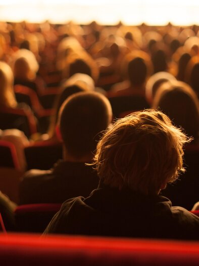 An audience is sitting in a large hall and looking at the stage. The people are in different positions, and the atmosphere is tense. | © AdobeStock_95665646.jpeg