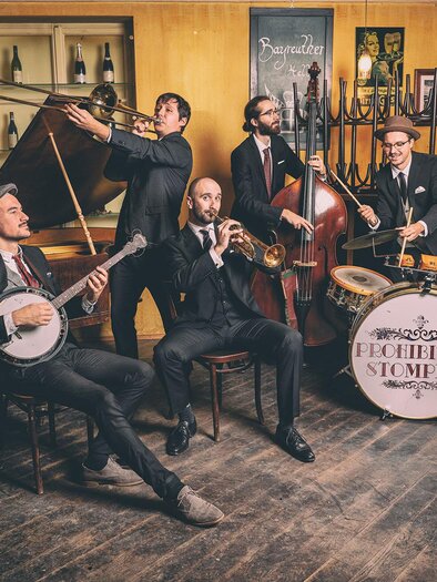 Drei Musiker stehen auf einer Bühne und spielen live Musik. Einer spielt Geige, während die anderen Gitarre spielen und singen. | © Reithofer