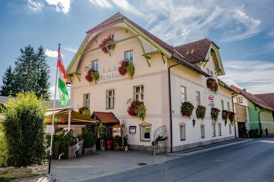 Ein charmantes Gebäude mit blühenden Pflanzen und einem einladenden Eingang. Die Straße vor dem Haus verleiht der Szenerie eine gemütliche Atmosphäre. | © KUK Wirtshaus