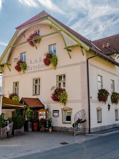 A charming building with blooming plants and an inviting entrance. The street in front of the house adds a cozy atmosphere to the scene. | © KUK Wirtshaus