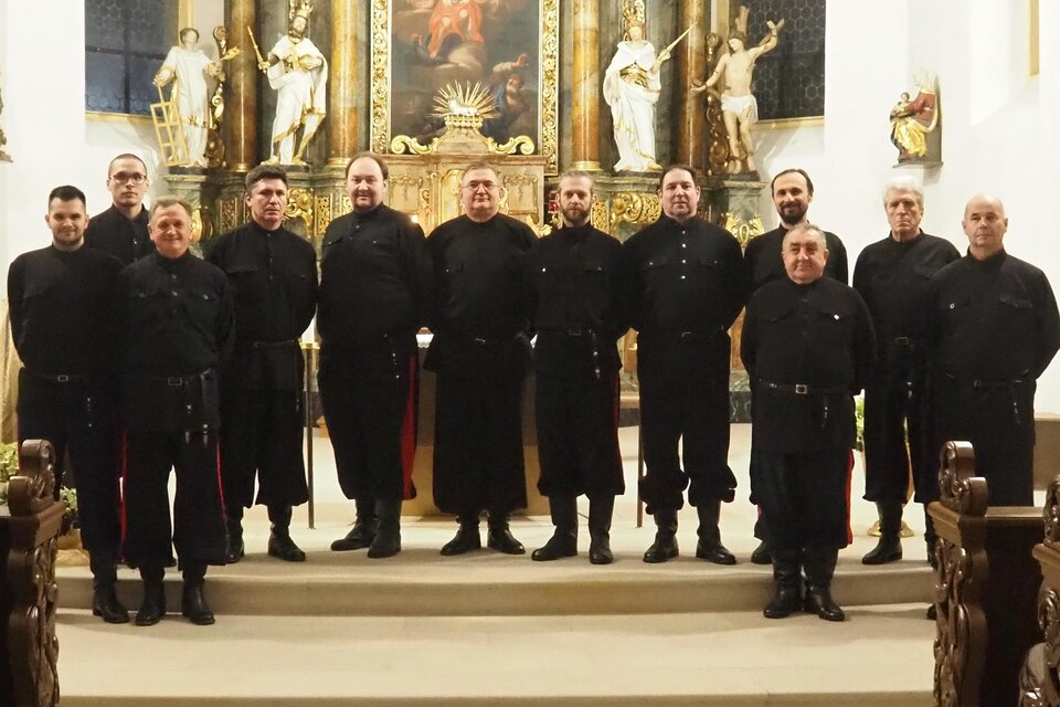 Eine Gruppe von Männern in schwarzen Kleidern steht vor einem kunstvoll verzierten Altar. Im Hintergrund sind religiöse Statuen und ein Gemälde sichtbar. | © DKCWH