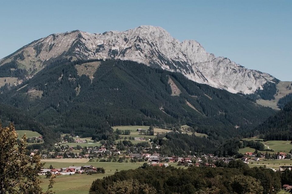 Eine beeindruckende Berglandschaft mit einem hohen Gipfel und grünen Tälern. Im Vordergrund sind kleine Dörfer und Wälder zu sehen. | © Leitner Stefan