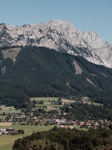 Eine beeindruckende Berglandschaft mit einem hohen Gipfel und grünen Tälern. Im Vordergrund sind kleine Dörfer und Wälder zu sehen. | © Leitner Stefan