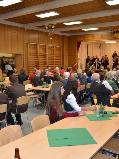 Eine Gesellschaft in einem großen Raum mit Tischen und Stühlen. Im Hintergrund spielt eine Band auf einer Bühne. | © Peter Fritz
