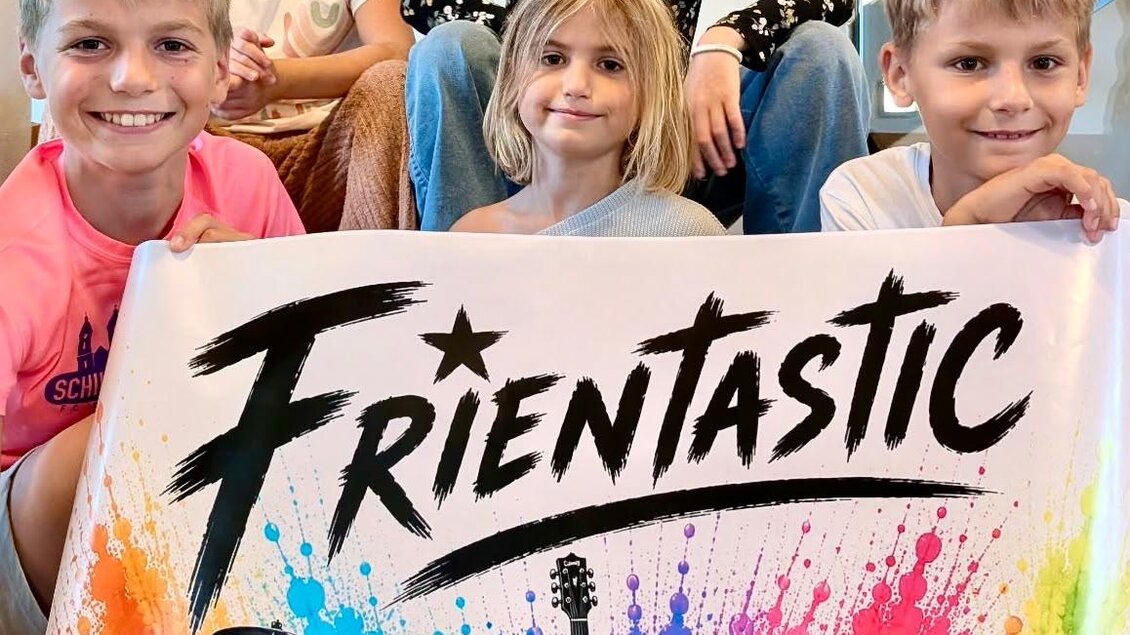Fünf Kinder sitzen lächelnd auf einer Treppe. Sie halten ein buntes Banner mit dem Schriftzug "FRIENTASTIC" und verschiedenen Musikinstrumenten. | © StainZeit - Julia Gruber