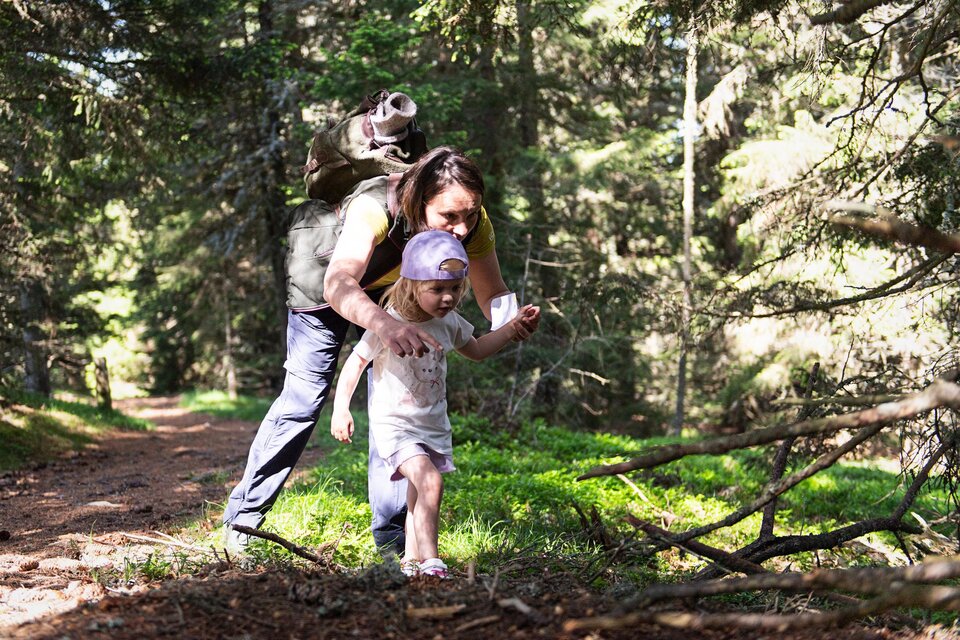 Eine Mutter und ihre Tochter gehen zusammen auf einem Waldweg. Die Tochter wird liebevoll von der Mutter begleitet und unterstützt. | © AlmDorf_Tonnerhütte