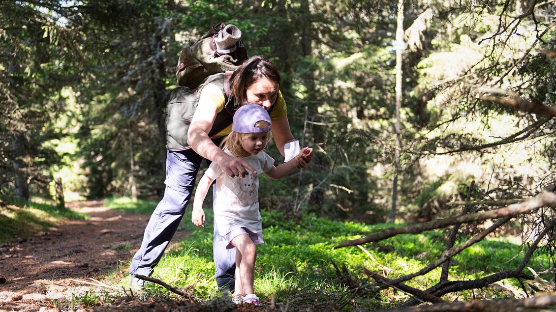Eine Mutter und ihre Tochter gehen zusammen auf einem Waldweg. Die Tochter wird liebevoll von der Mutter begleitet und unterstützt. | © AlmDorf_Tonnerhütte