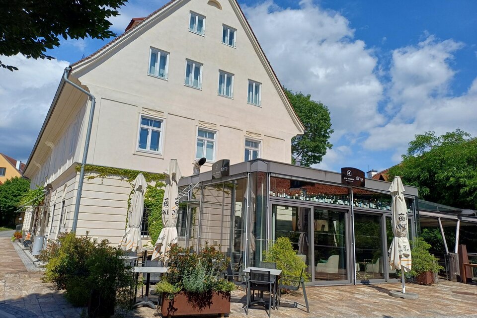 Ein charmantes Café mit einer großen Glasfassade und Außensitzplätzen. Umgeben von Bäumen und einem klaren blauen Himmel. | © TV Südsteiermark - Löschnig Irene