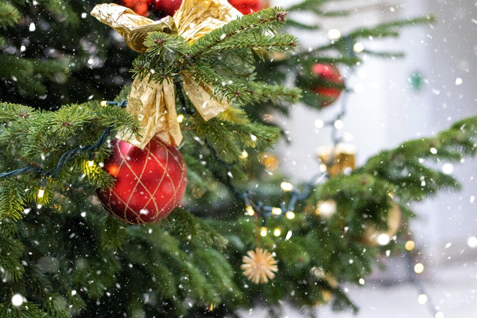 Ein geschmückter Weihnachtsbaum mit roten und goldenen Kugeln. Es fällt sanfter Schnee, während Lichter den Baum erhellen. | © Liviu-c