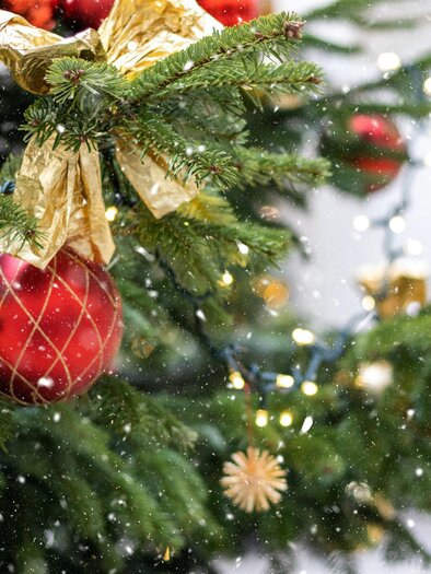 Ein geschmückter Weihnachtsbaum mit roten und goldenen Kugeln. Es fällt sanfter Schnee, während Lichter den Baum erhellen. | © Liviu-c