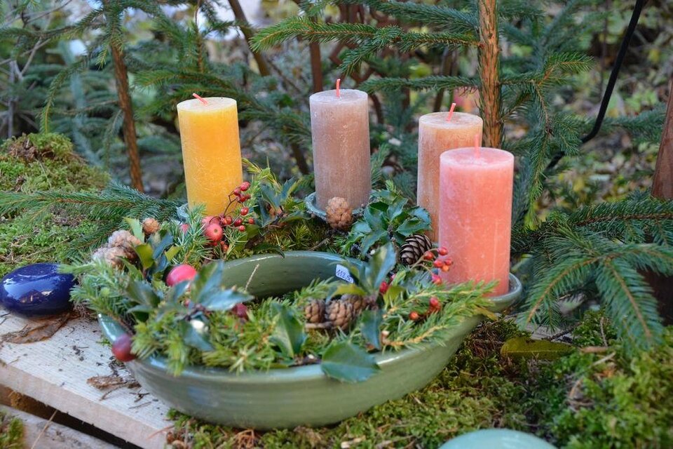 Ein dekorativer Adventskranz mit fünf Kerzen in verschiedenen Farben. Der Kranz ist mit grünen Zweigen und kleinen Beeren geschmückt. | © Maria Wabnegg-Eberl