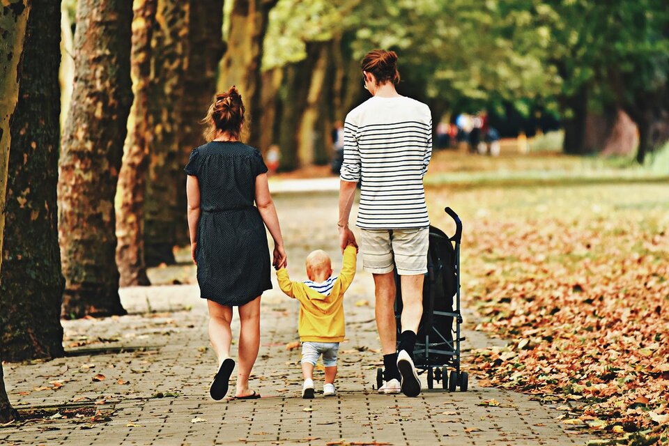 Ein Paar mit einem kleinen Kind spaziert auf einem Weg zwischen Bäumen. Das Kind hält die Hände der Eltern und trägt einen gelben Pullover. | © Bild: freepik