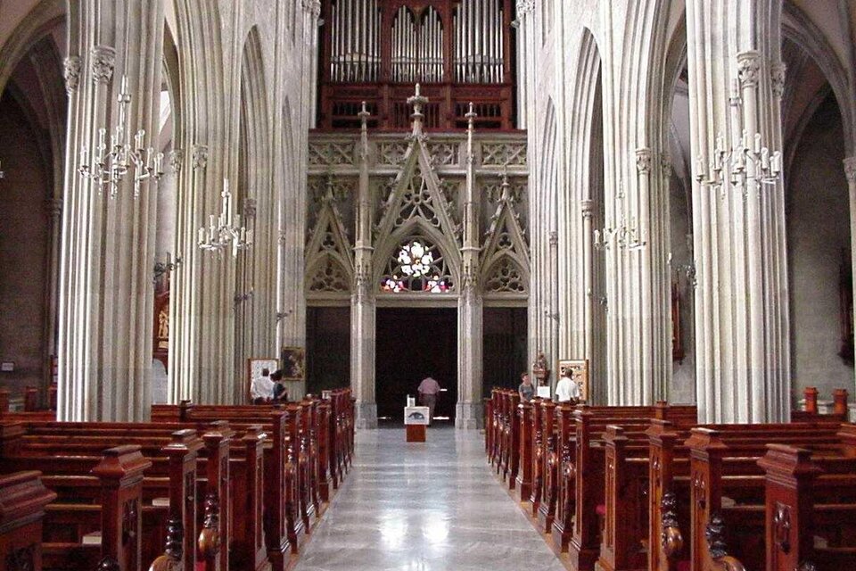 Eine beeindruckende Kircheninneneinrichtung mit hohen gewölbten Decken und eleganten Holzbänken. Im Hintergrund befindet sich eine große Orgel und ein schönes Kirchenfenster.
